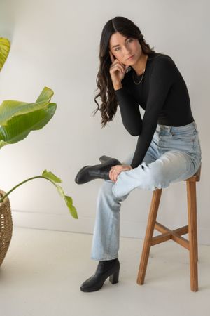 Professional lifestyle photo series showing someone seated on a wooden stool wearing jeans and a black sweater.
