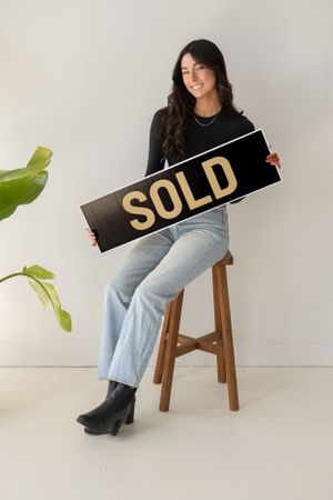 Model posing with sold signs in a minimalist studio setting with light denim and black attire.