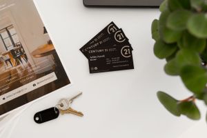 Business cards and interior design materials arranged with greenery on white surface.