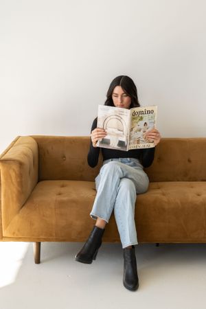 Casual reading scene on a camel-colored modern sofa against white wall.