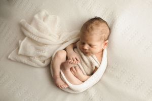 Tranquillo neonato che dorme su una coperta bianca testurizzata durante un servizio fotografico professionale.