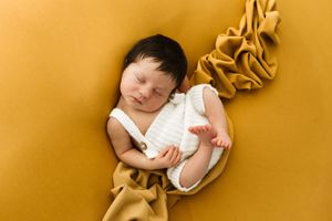 Fotografia Newborn di una bimba che dorme serenamente su sfondo giallo ocra e tessuto morbido abbinato. nel mio studio a Cassine.