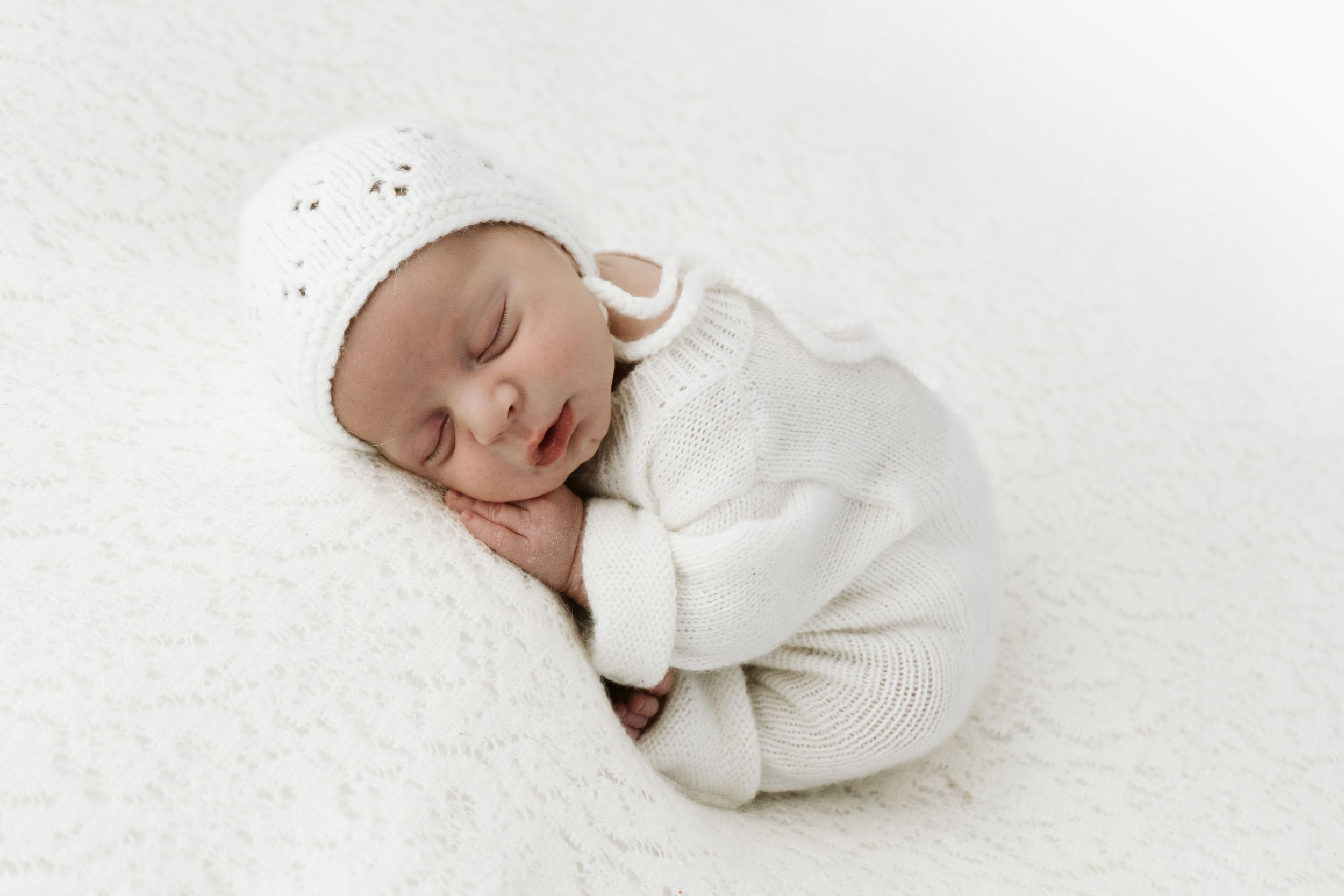 Neonato che indossa un vestito bianco durante la sessione di fotografia professionale in studio a Cassine.