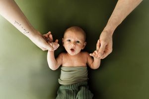Fotografia Oldborn di un bimbo di un mese con le mani dei suoi genitori.