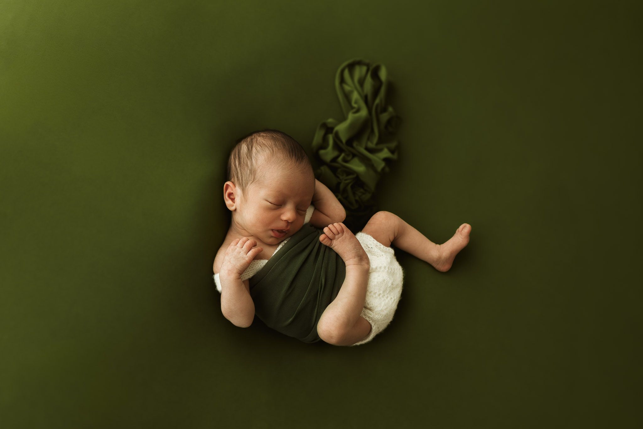 Dolce fotografia newborn di una bimba posizionata elegantemente ed in maniera naturale su sfondo verde con drappi verdi.