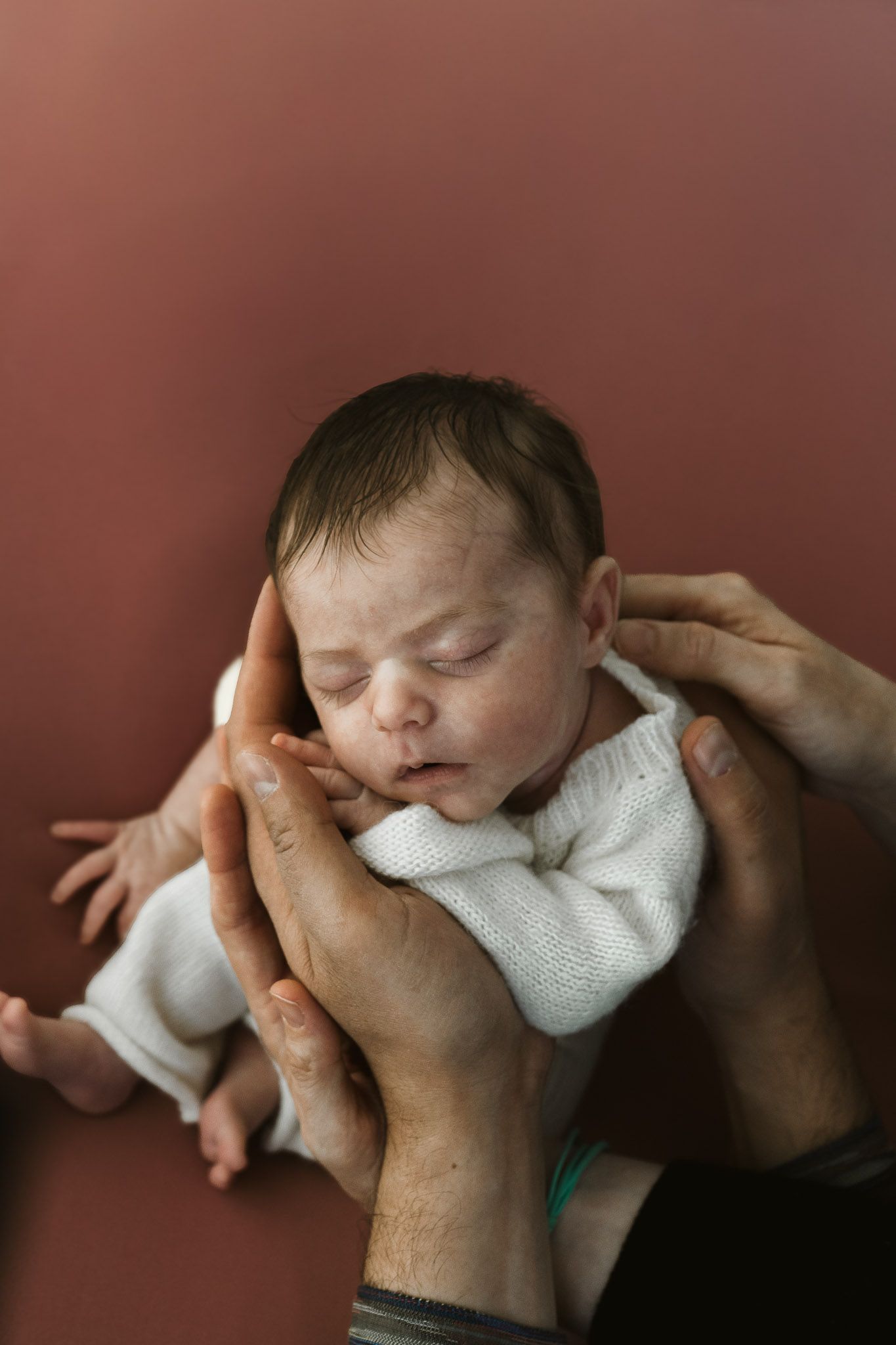 Fotografia newborn di una neonata che dorme sorretta dalle mani dei suoi genitori su sfondo rosa.