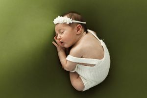 Fotografia newborn di una neonata che dorme su sfondo verde e cordoncino di fiori.