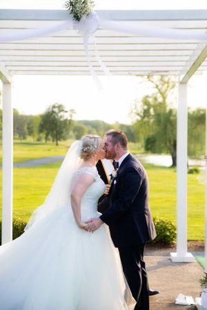 Wedding couple shares intimate moment under white pergola on golf course.