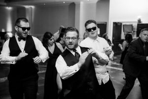 Groomsmen in formal attire dancing and celebrating at a wedding reception.