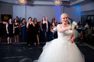 Bride in white ball gown tosses bouquet to waiting crowd at reception.