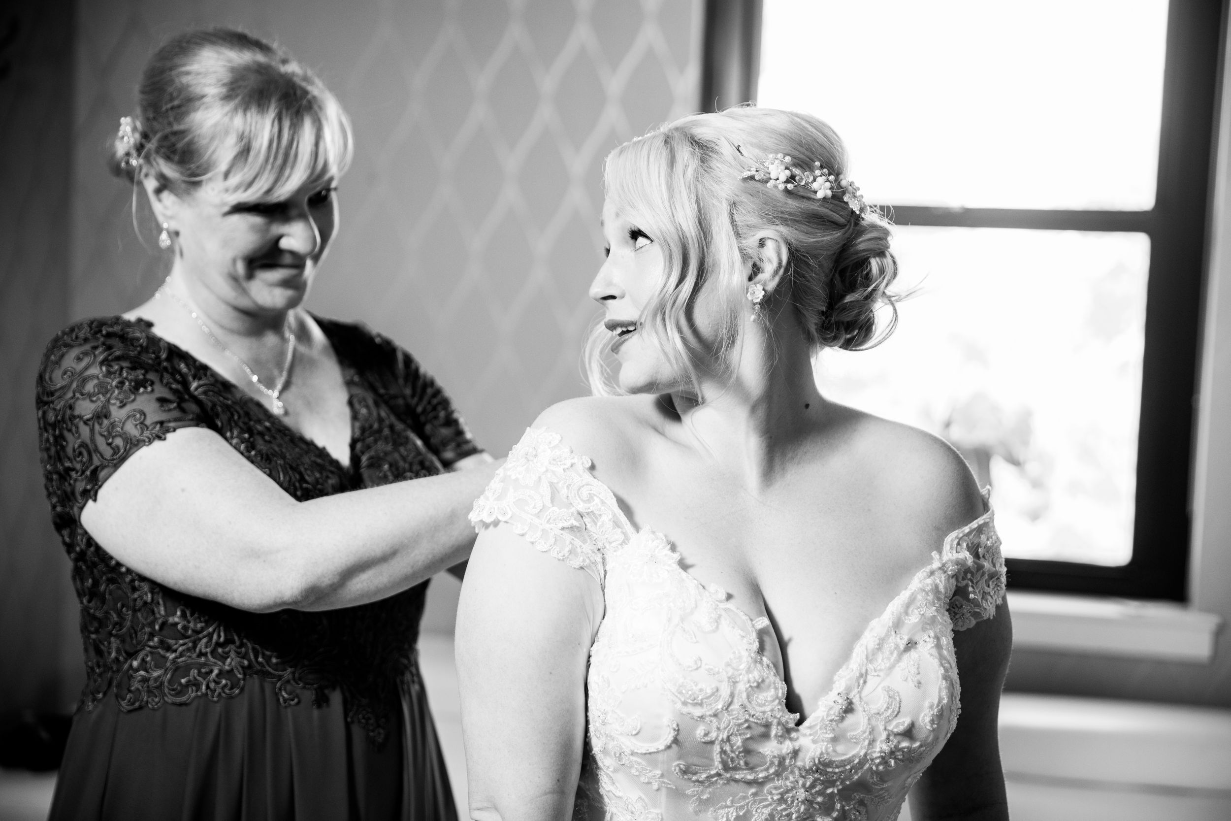 Getting ready moment shows final wedding dress adjustments in black and white photography.