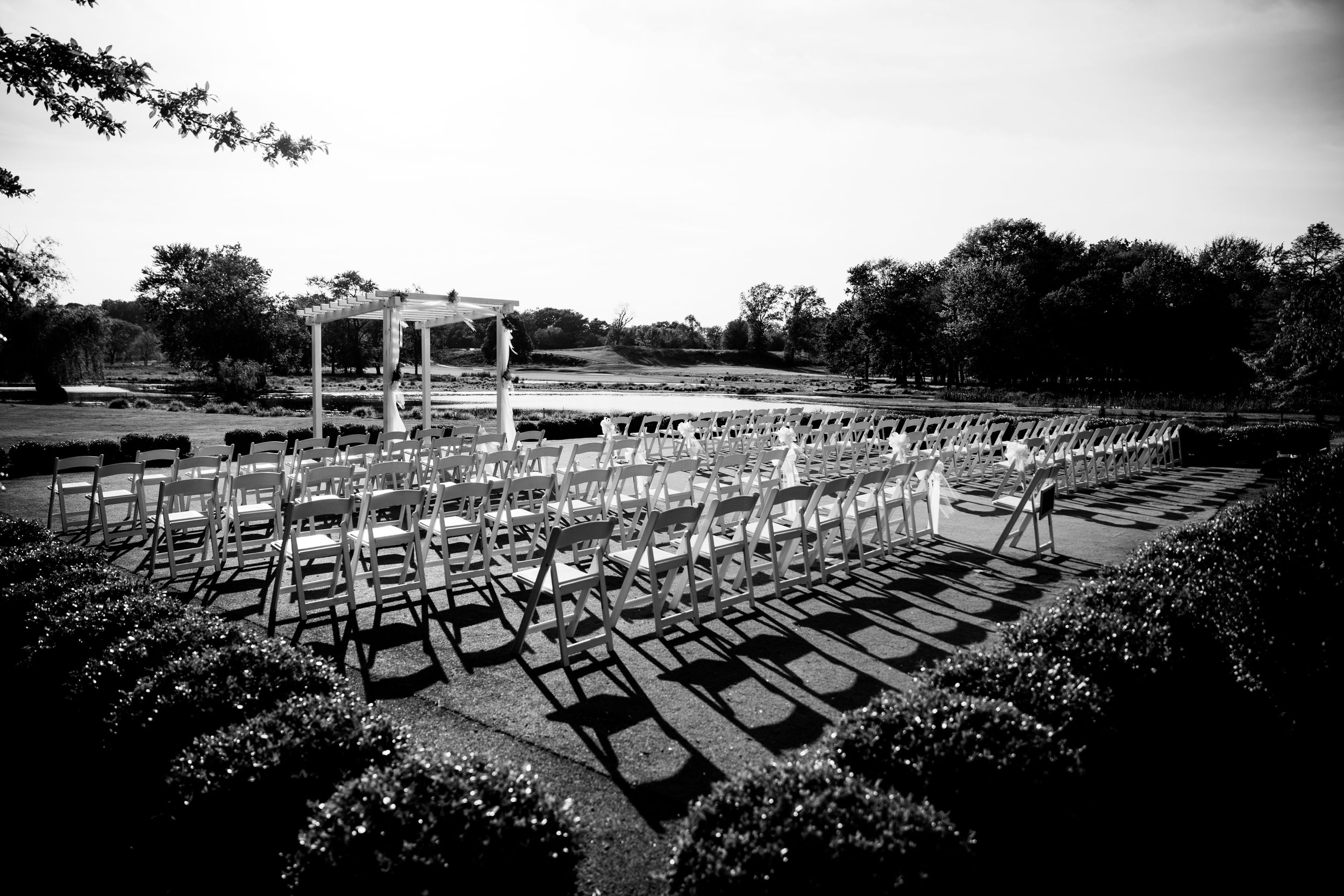 Black and white photo of outdoor wedding ceremony setup with rows of white chairs.