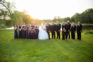 Wedding party poses on green lawn with bridal couple in center.