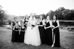 Wedding party photo with bridesmaids in black dresses gathered outdoors.