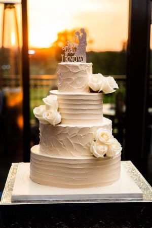 Elegant four-tier white wedding cake decorated with fresh roses and a cake topper.