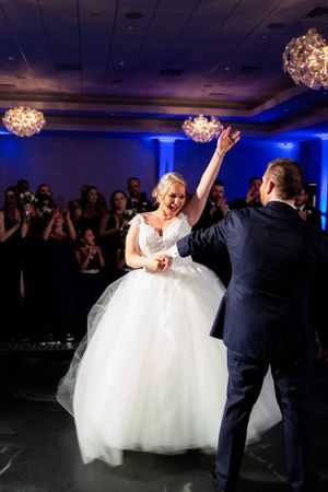 Bride and groom perform energetic dance move at reception under crystal chandeliers.