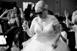 Candid photo of a bride wearing sunglasses and holding champagne while dancing.