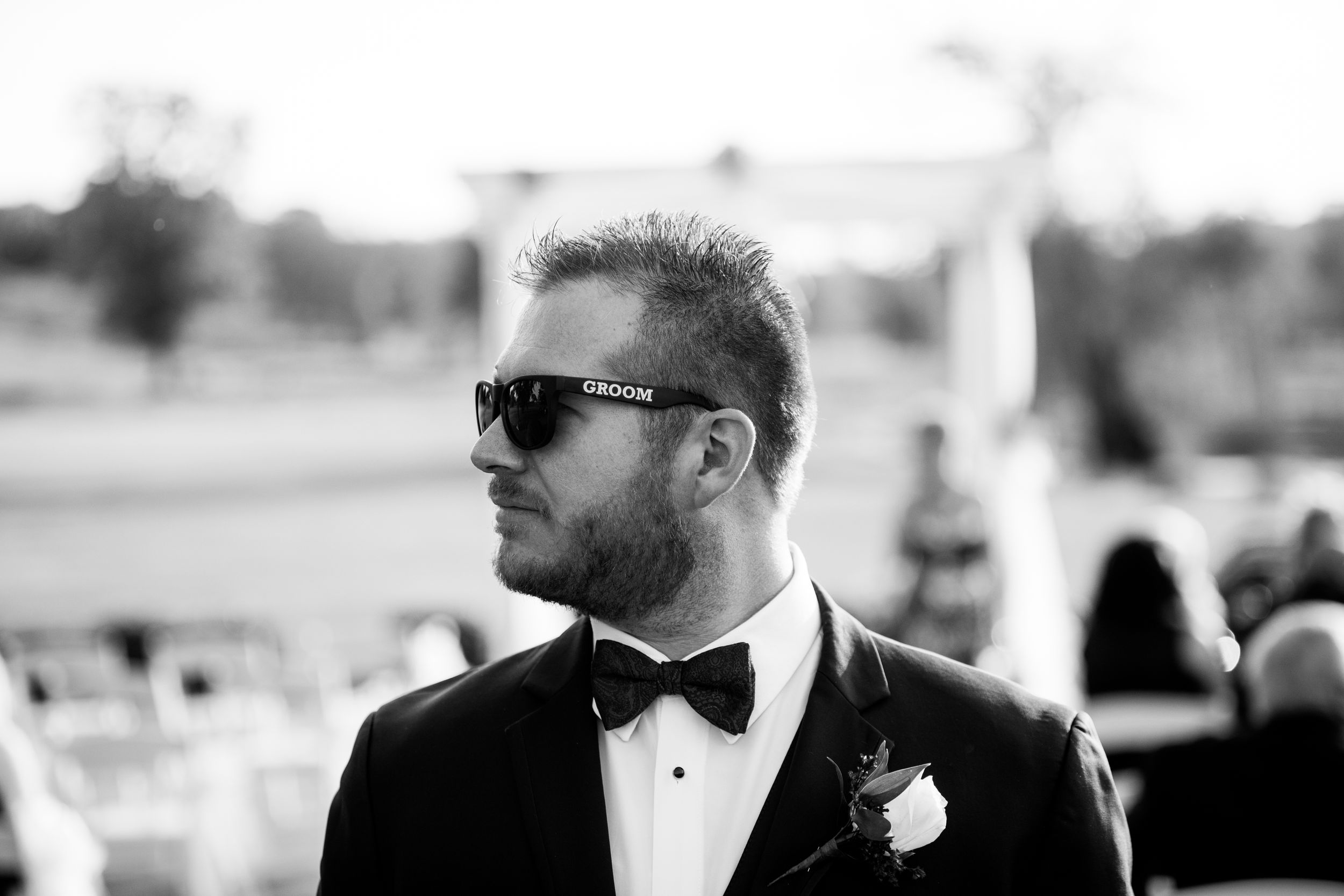 Classic black and white portrait of a groom in tuxedo and sunglasses outdoors.