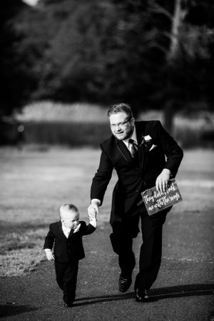 Parent and child walking hand in hand at a wedding, both in formal attire.