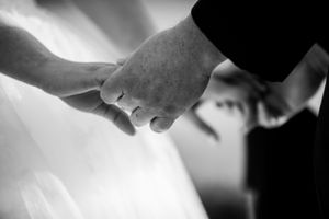 Black and white close-up of newlyweds holding hands showing wedding rings.