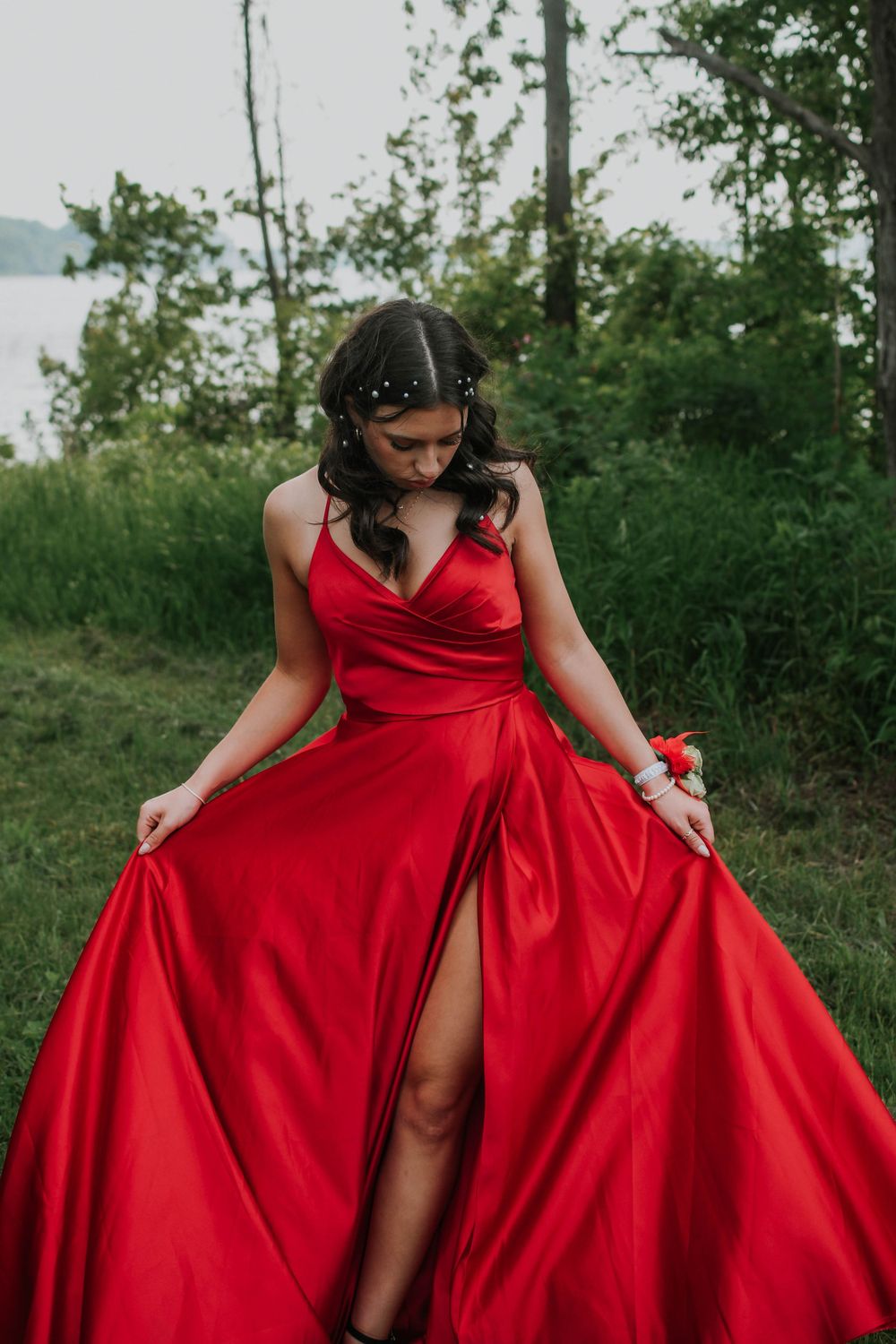 Elegant red satin evening gown with thigh slit photographed outdoors against natural green foliage.