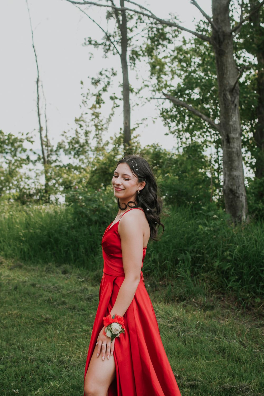 Elegant red formal dress photographed in outdoor natural setting with trees and grass in background.