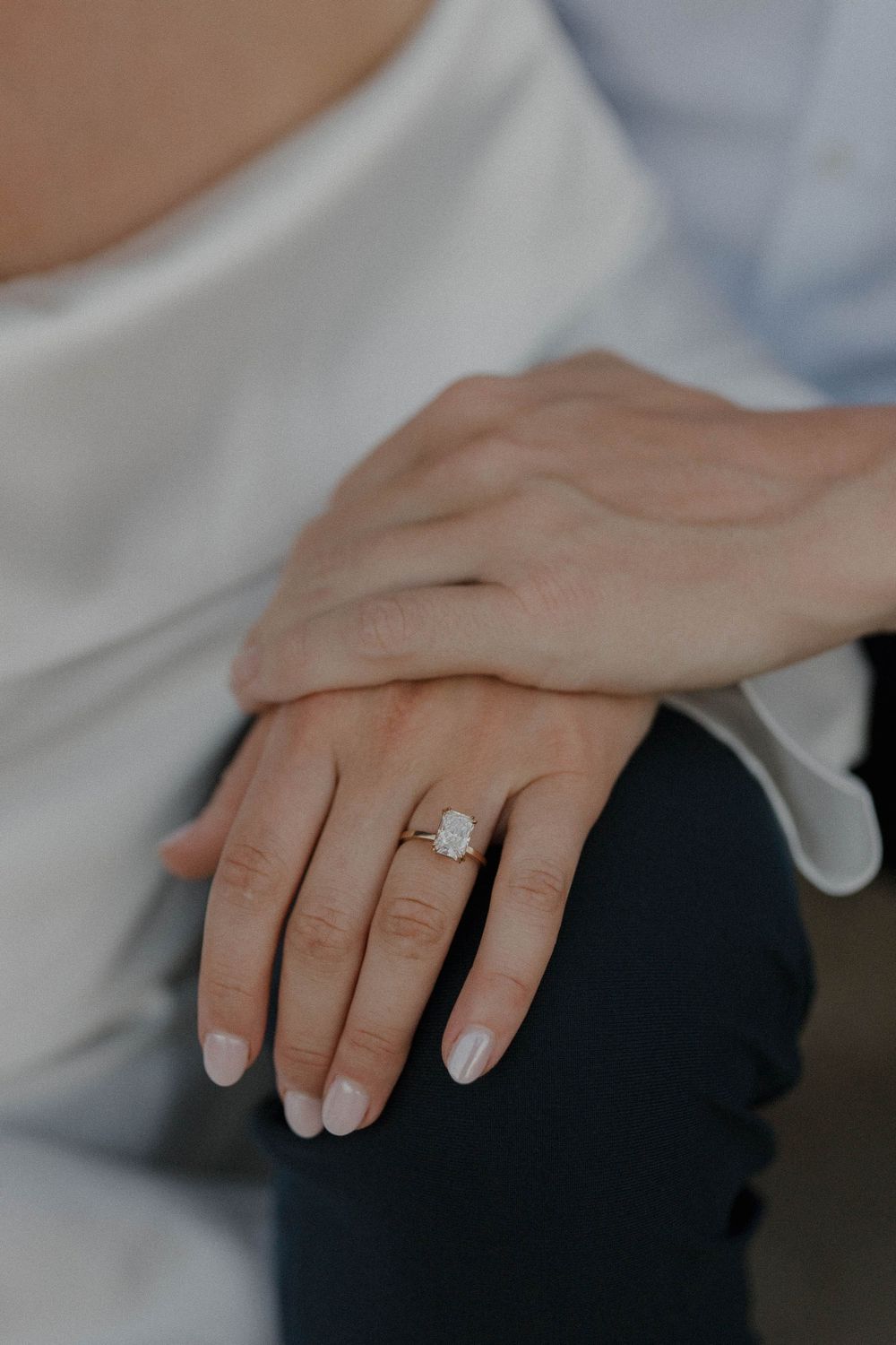 A hand wearing an engagement ring rests gently against dark fabric.