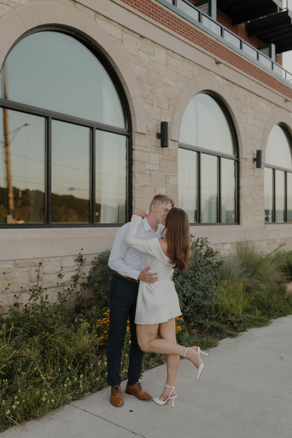 A romantic moment captured outside a building with arched windows and stone facade.