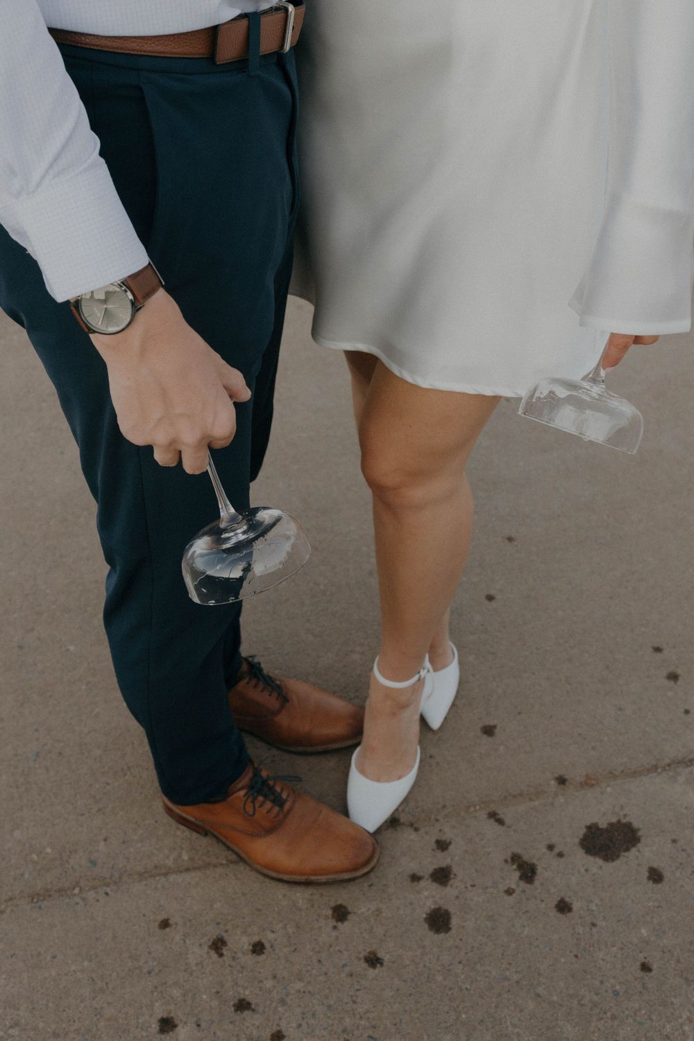 Close-up of couple's feet showing brown leather shoes and white heels.