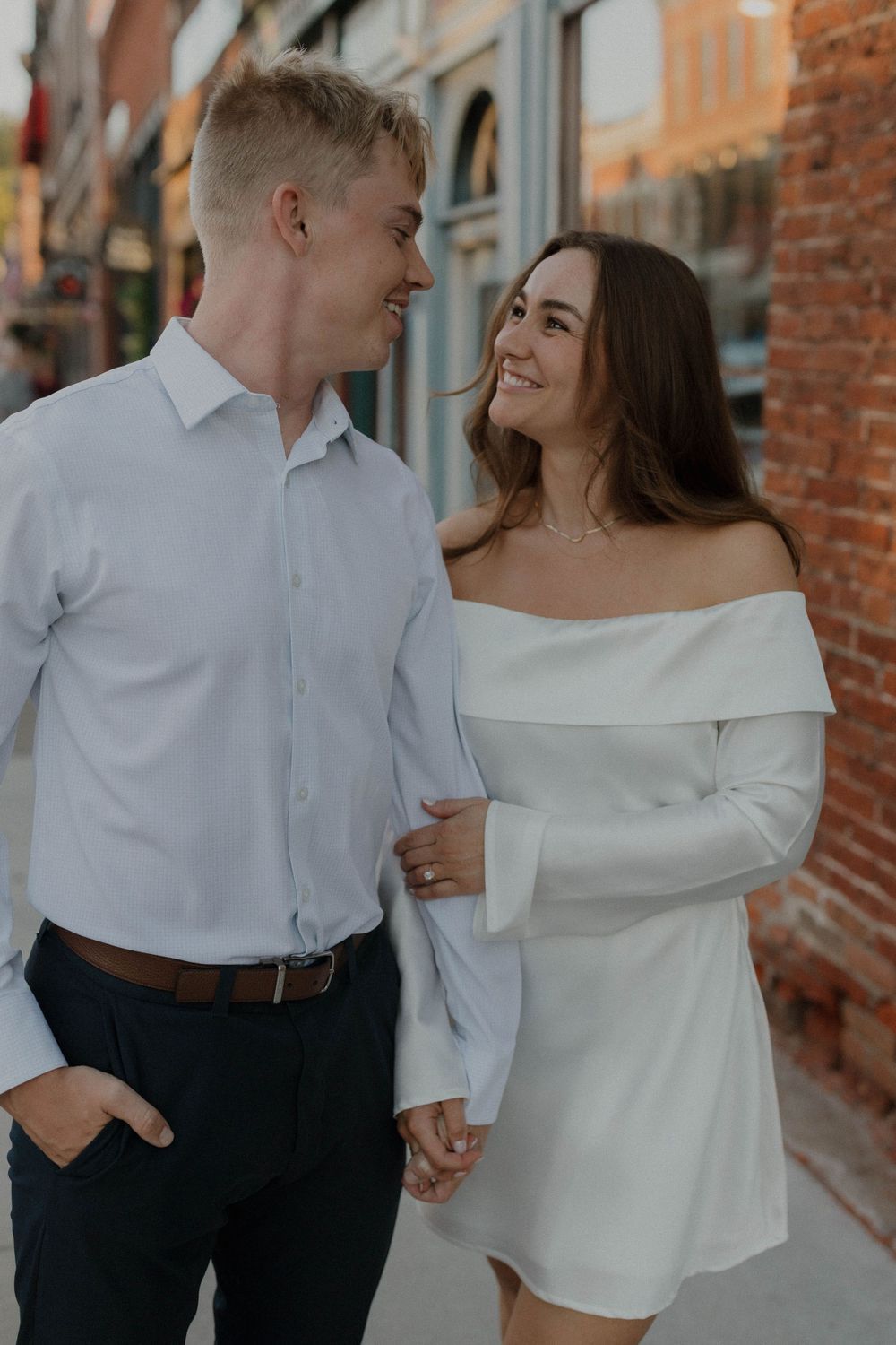 Couple in coordinated white and formal wear walking along brick building exterior.