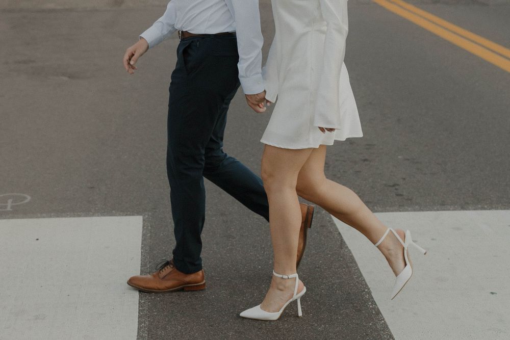 Close-up of feet walking across a crosswalk, showing dress shoes and white heels.