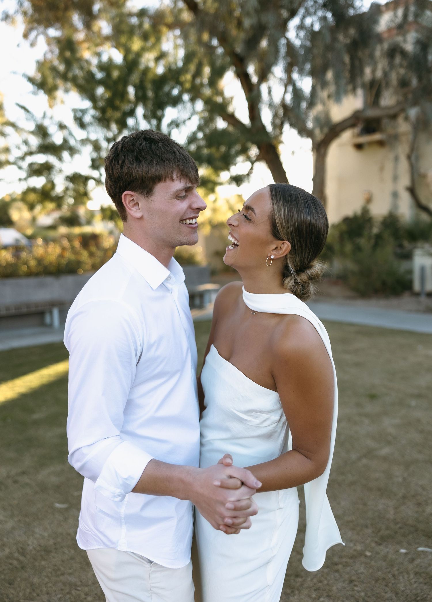 A couple in white outfits sharing a joyful moment outdoors at sunset.