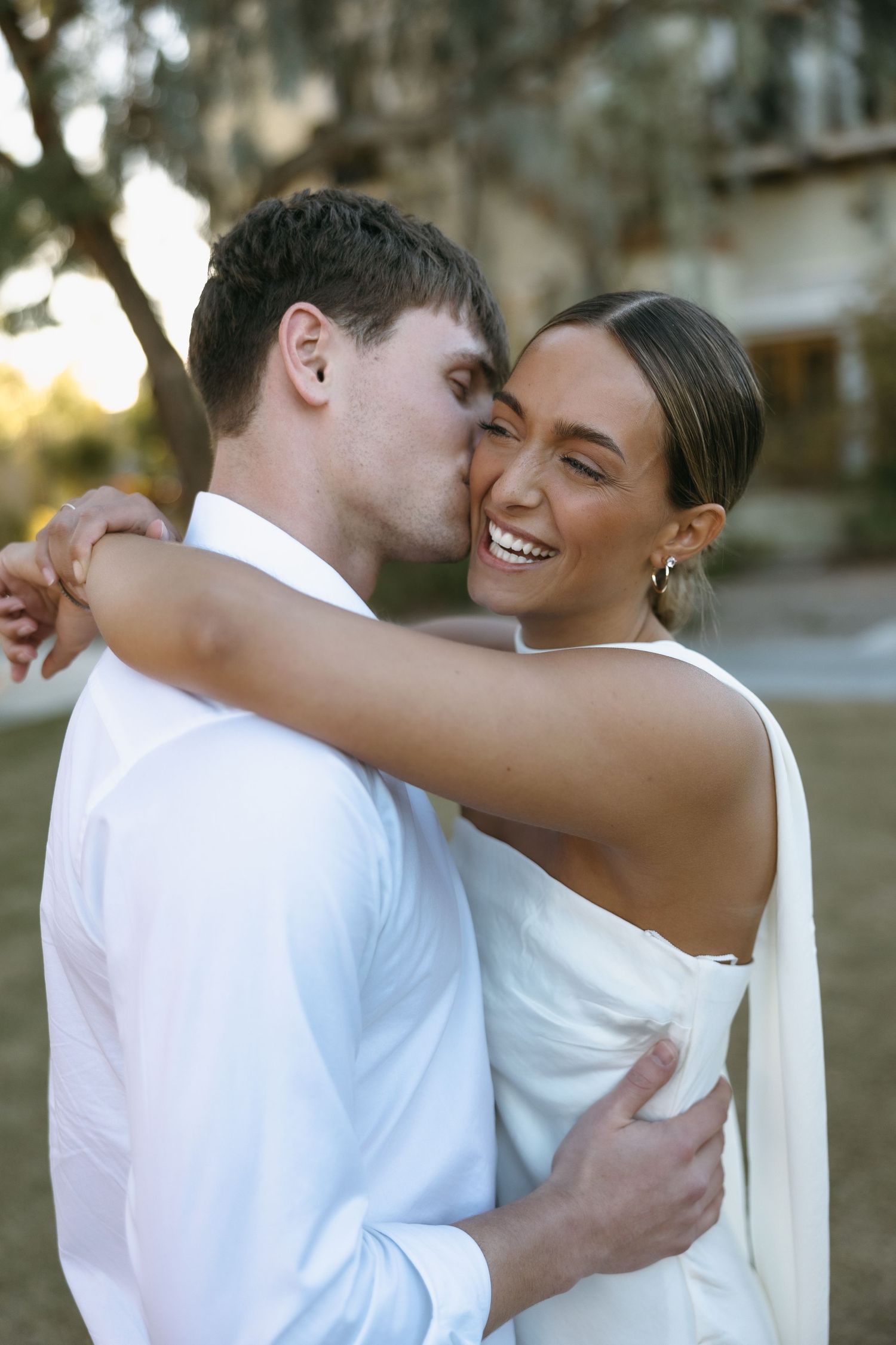 A tender moment between a couple dressed in white as they embrace outdoors.