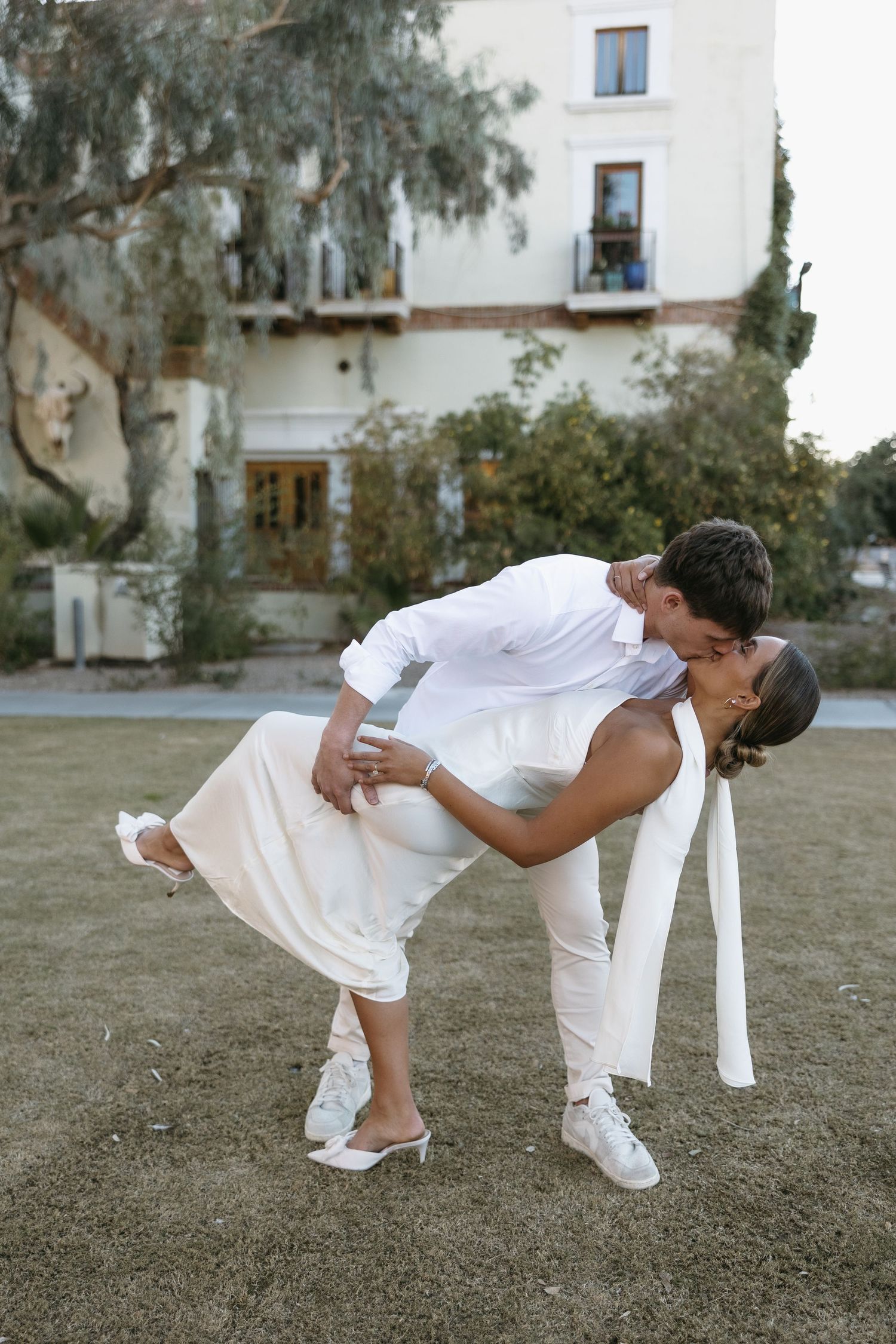 A romantic dip pose between a couple dressed in all white outside a building.