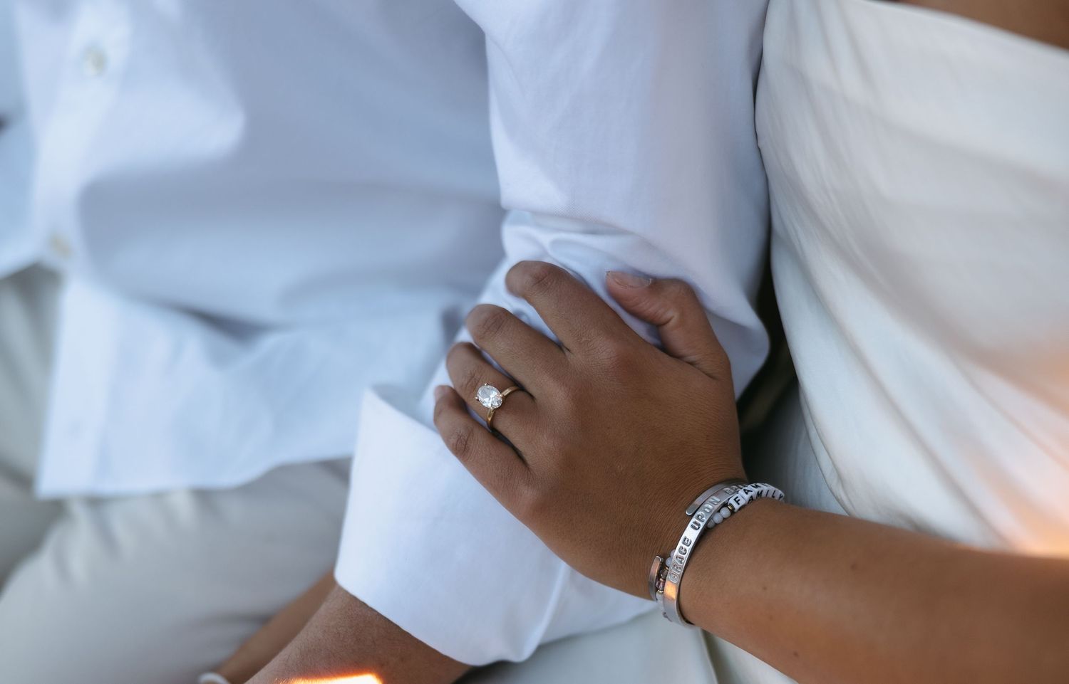 A close-up shot of hands with wedding rings and a bracelet against white formal attire.