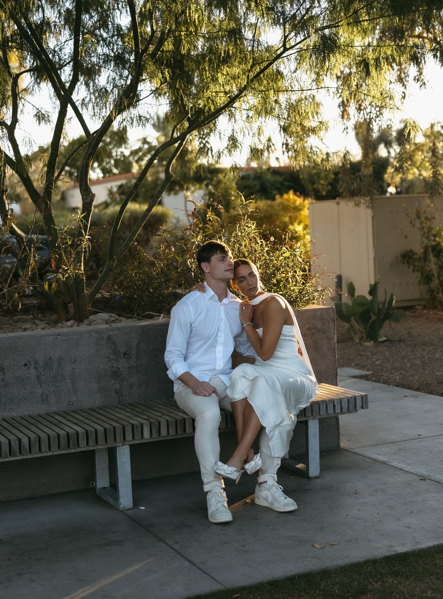 A couple in white outfits sitting together on a bench during golden hour.