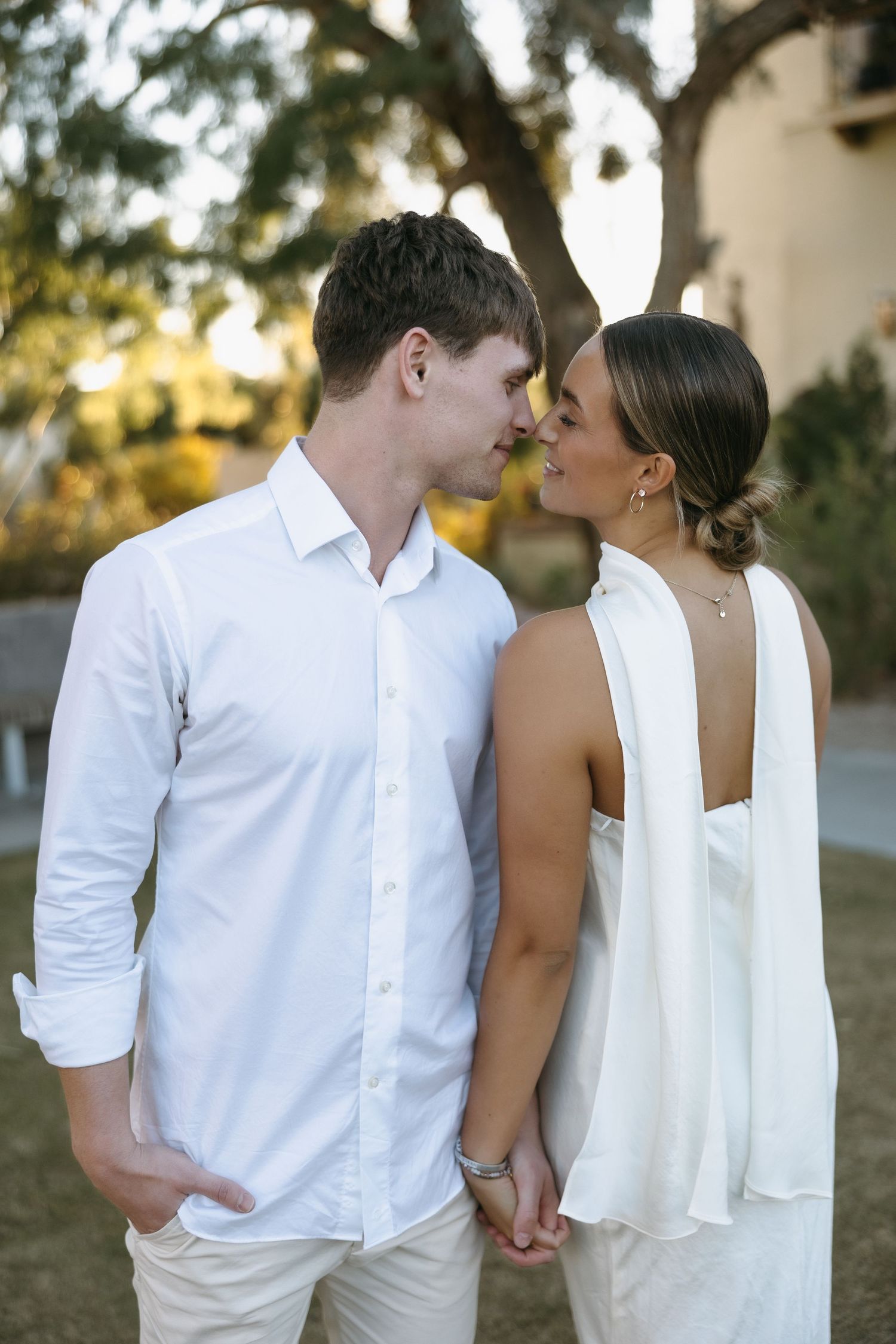 A romantic moment between a couple in matching white outfits against a natural backdrop.