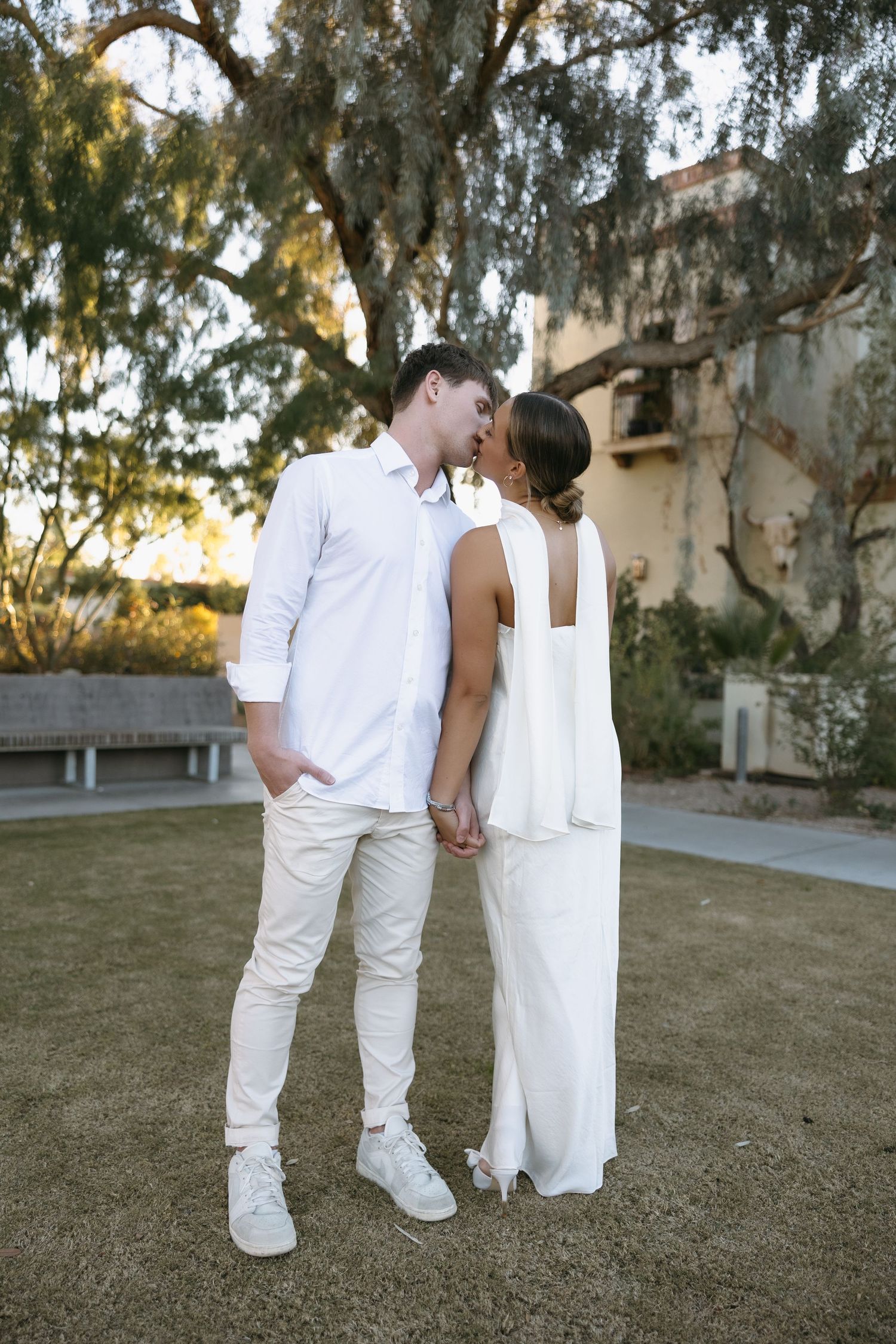 A tender moment between a couple dressed in white against a garden background at sunset.