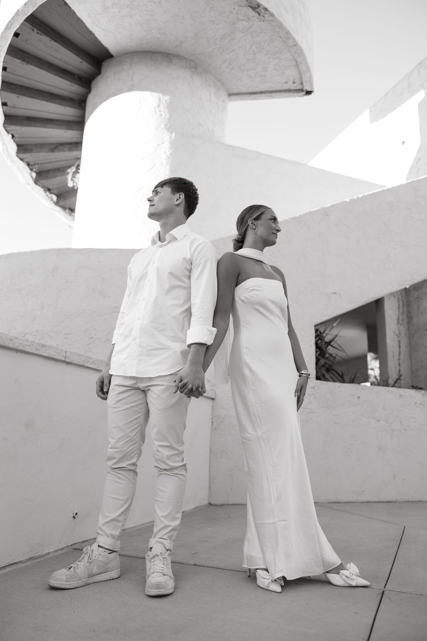 Black and white portrait of couple standing back to back on modernist architectural terrace.