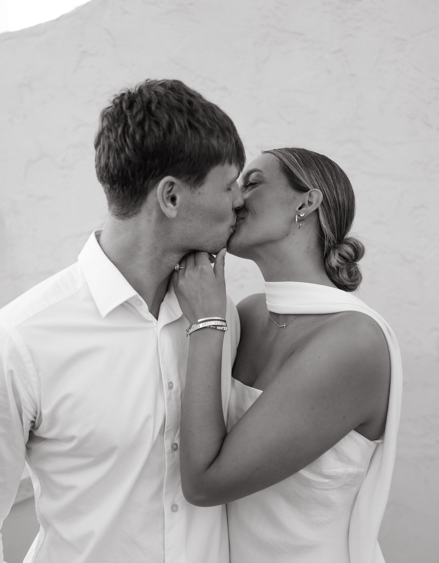 A romantic black and white photo of a couple sharing an intimate kiss while dressed in white.