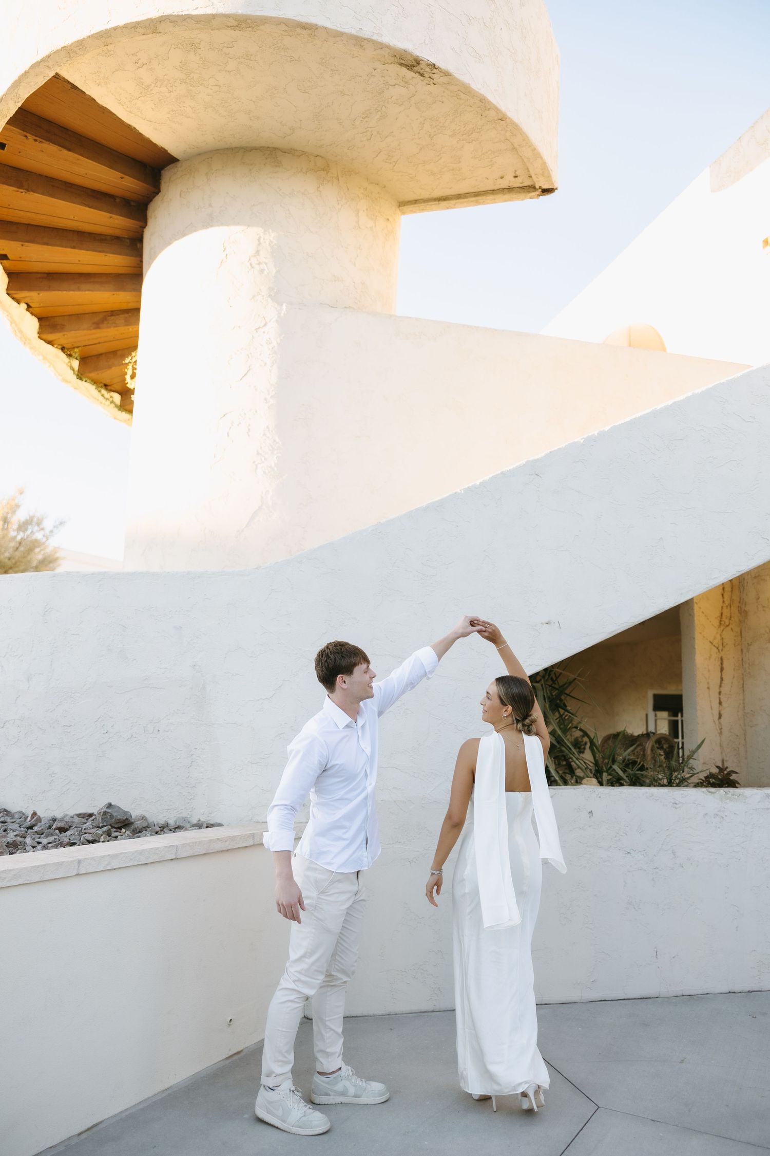 A couple in white outfits dancing together under a modern architectural overhang.