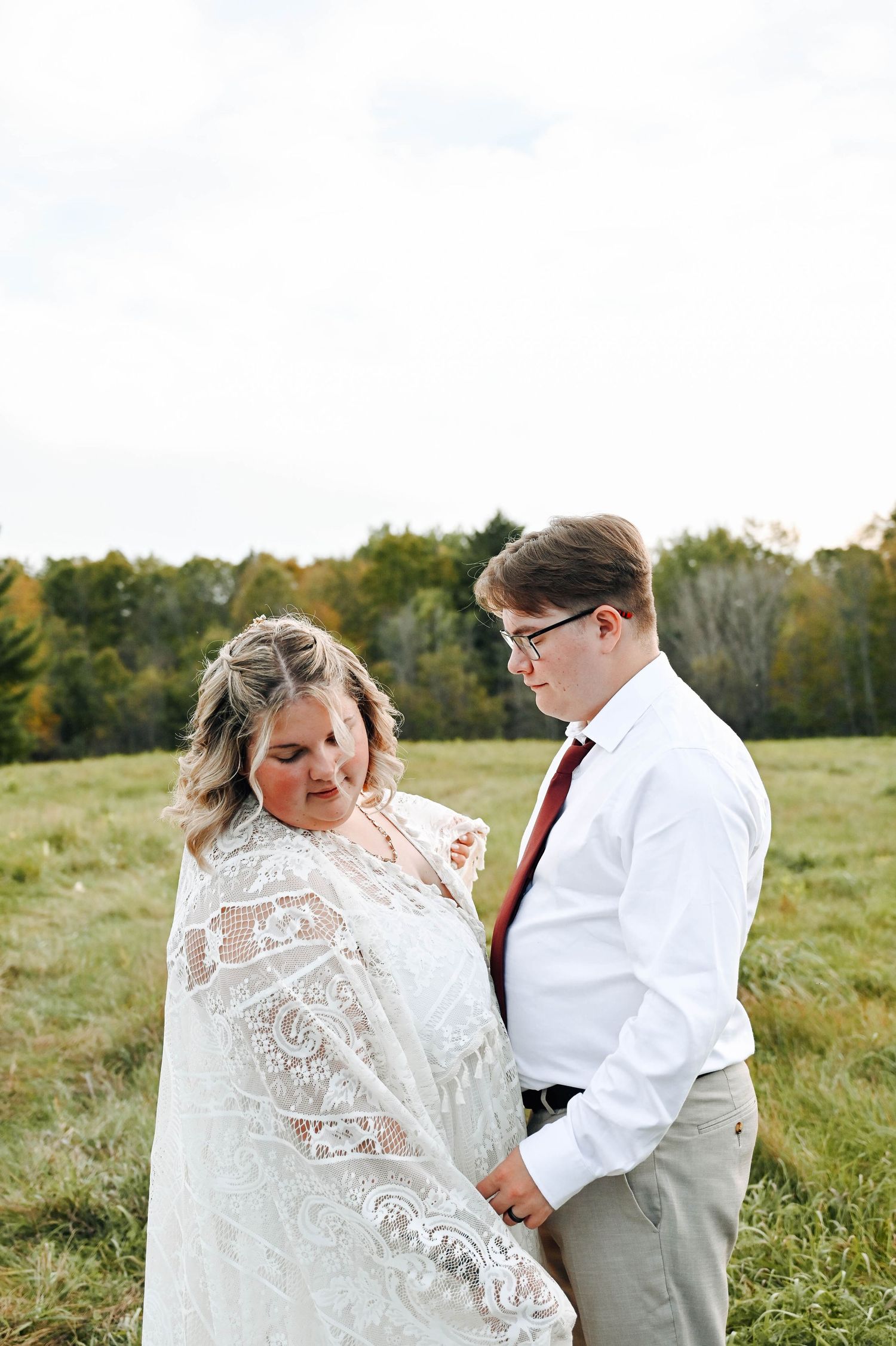 A couple shares an intimate moment in a sunny field wearing white and formal attire for their wedding photos.