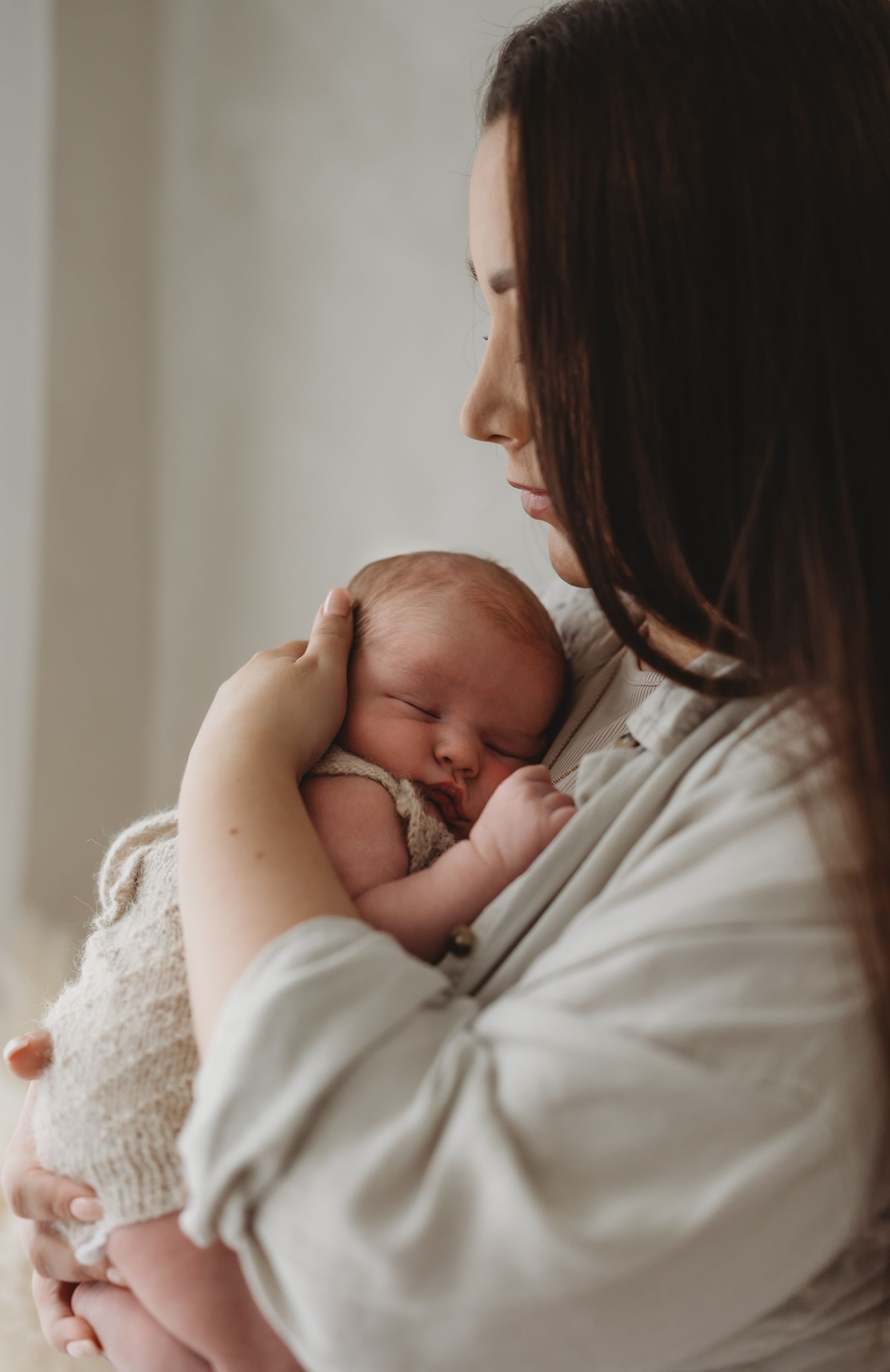Leicestershire newborn photography studio. A tender moment captured as a newborn baby rests peacefully against Mum wearing a white robe.