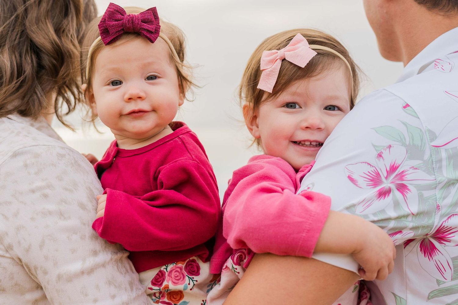 Children wearing pink bows sitting together on coastal rocks during family photoshoot.