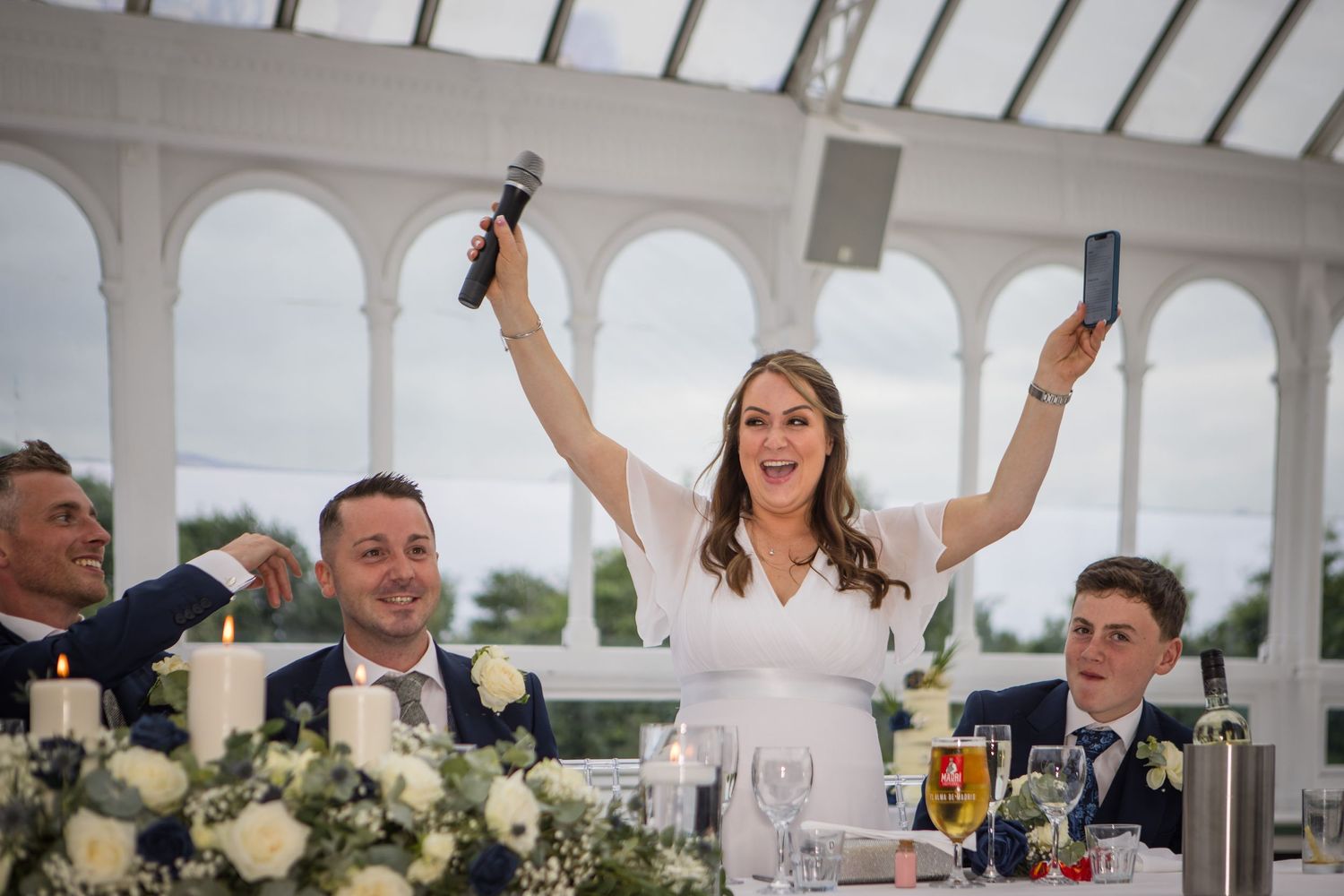 Wedding guests celebrating inside bright conservatory with arched windows and decorative details.