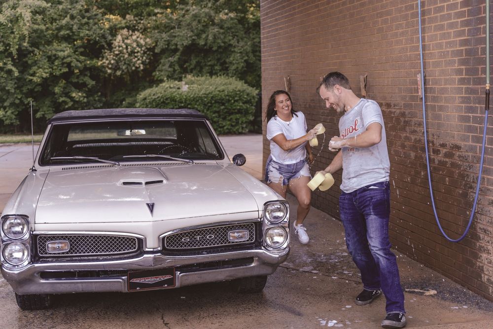 Married couple playfully running in a car wash during a lifestyle session in Charlotte, North Carolina