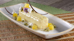 Artfully plated yellow petals garnish a white creamy dessert on an elegant elongated serving dish.