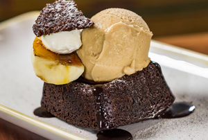 Freshly baked chocolate brownies topped with ice cream scoops and banana slices on a white plate.
