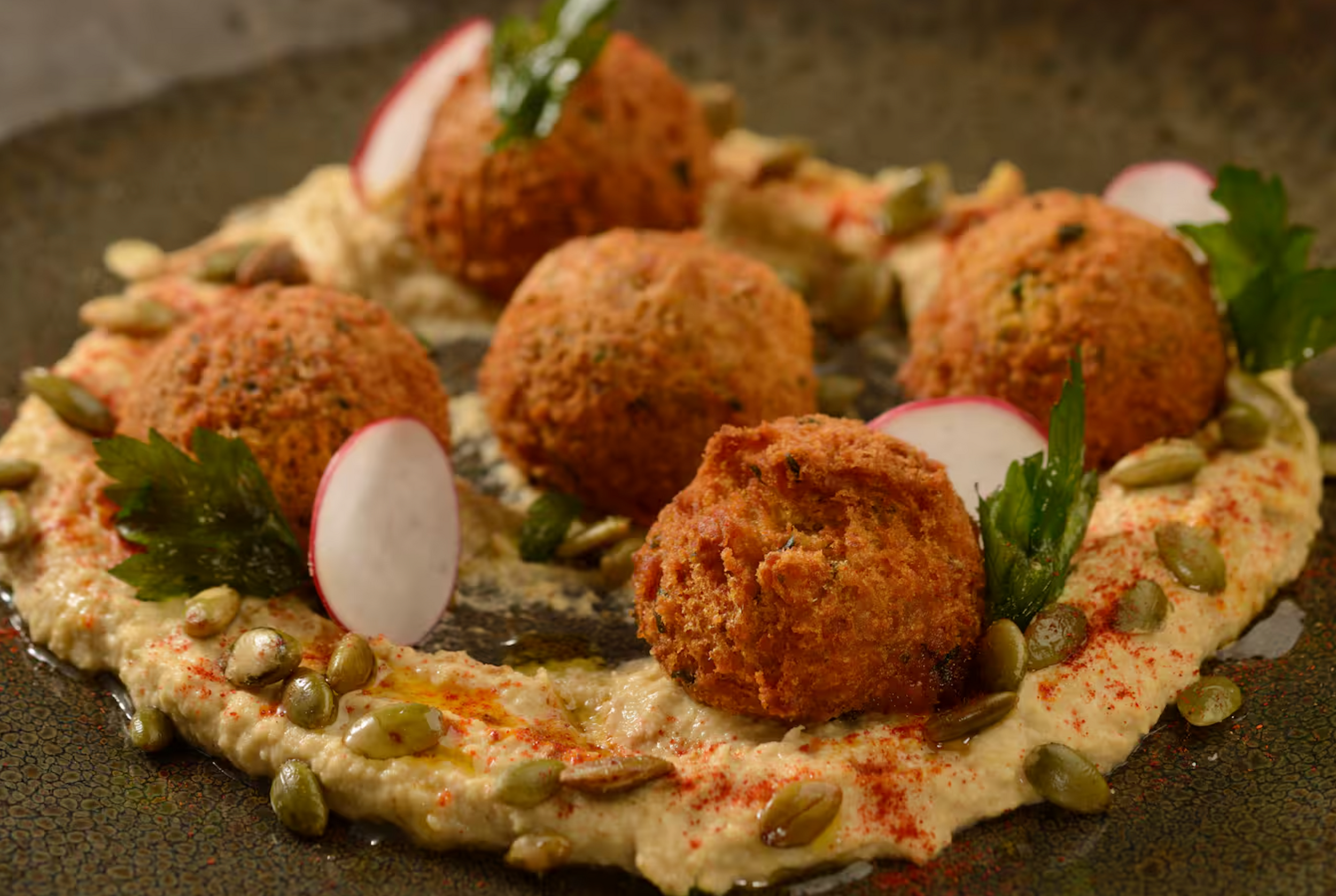 Crispy falafel balls served on a bed of hummus garnished with radish slices and fresh herbs on a rustic plate.