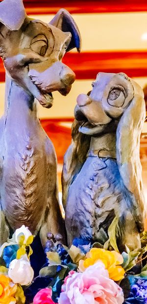 Two cartoon-style dog statues facing each other surrounded by colorful flowers with a red and white striped background.